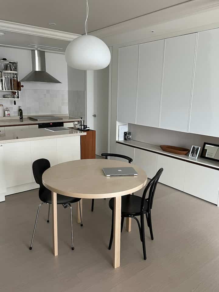 Modern kitchen space with white and wood tones, featuring a round dining table and black dining chairs arranged neatly