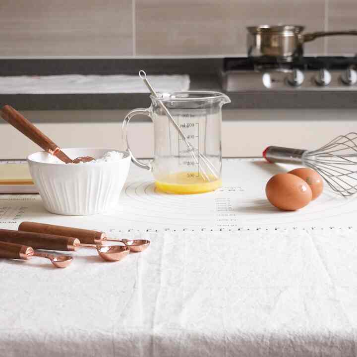 白とナチュラルカラーのキッチン、計量カップや泡立て器などの調理器具が配置された清潔感のある空間