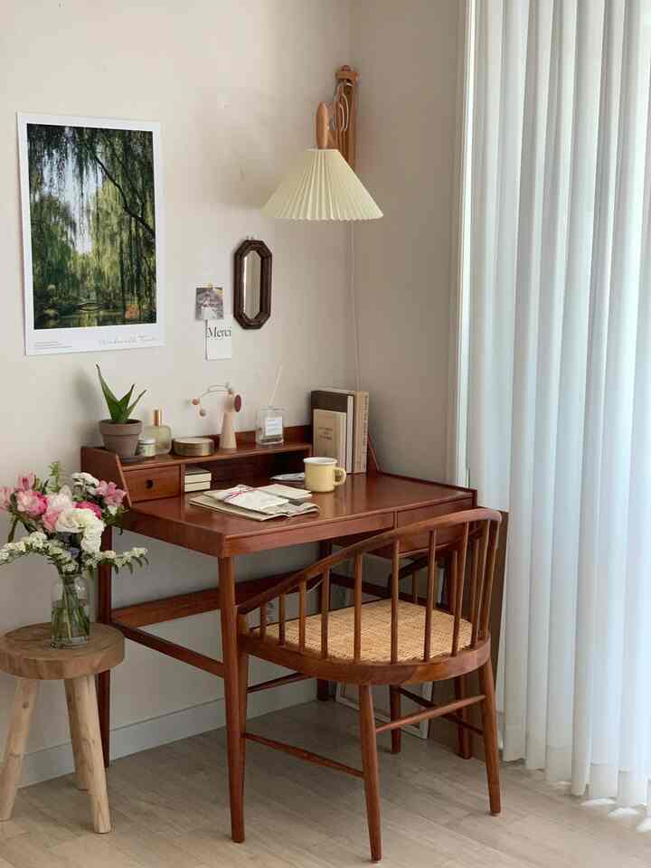 Natural wood tone home office space featuring wooden desk, rattan chair, and stool with flower vase, creating a cozy, neat workspace