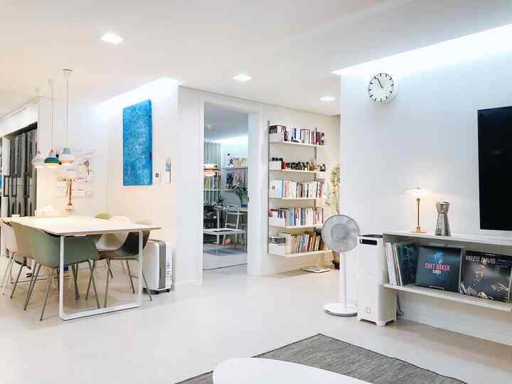 Bright white-toned living and dining room featuring clean modern furniture and a bookshelf, creating a neat atmosphere