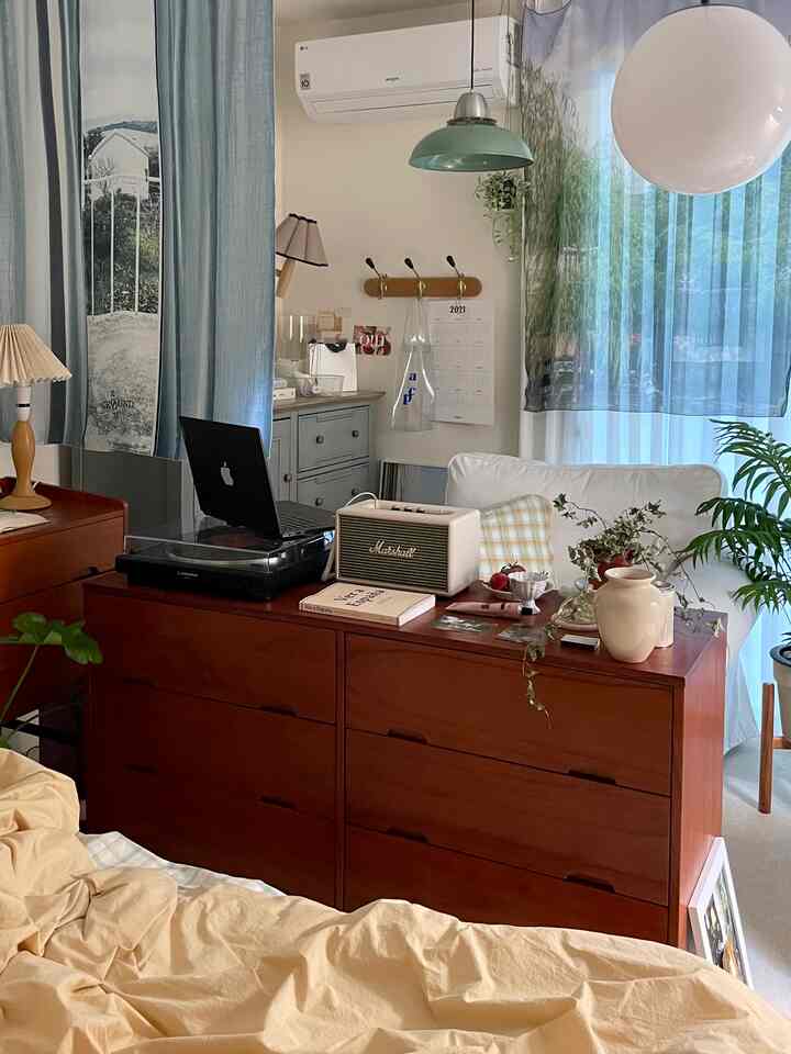 A cozy bedroom in white and wood tones featuring a large dresser at center and a sofa by the window