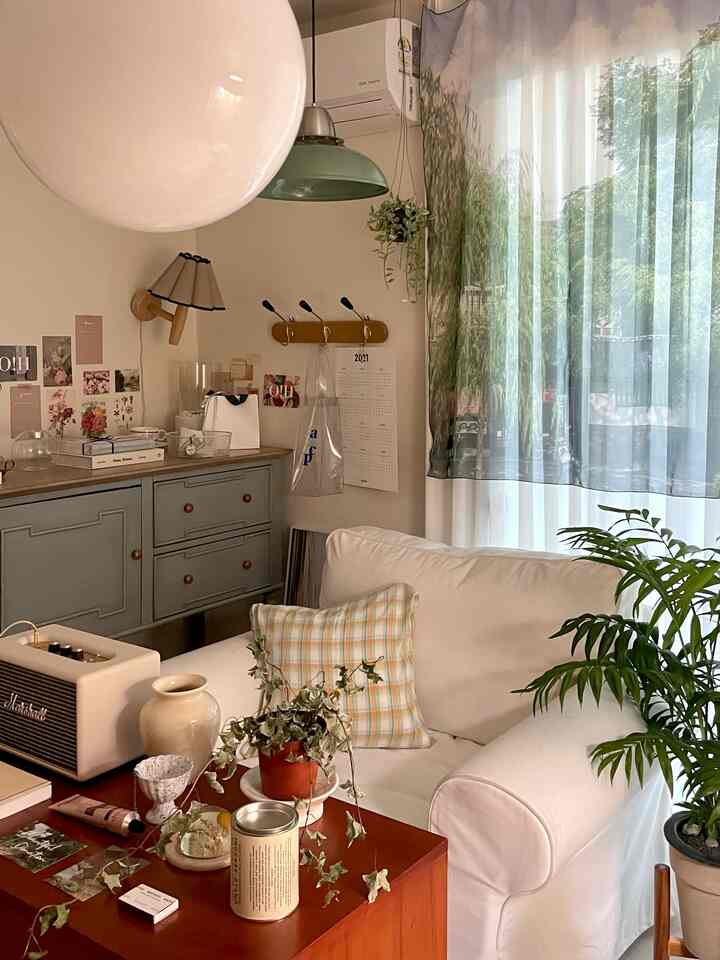 Beige natural-toned studio apartment living room featuring a white armchair with checkered cushion, wood-toned coffee table, and plants creating a cozy atmosphere