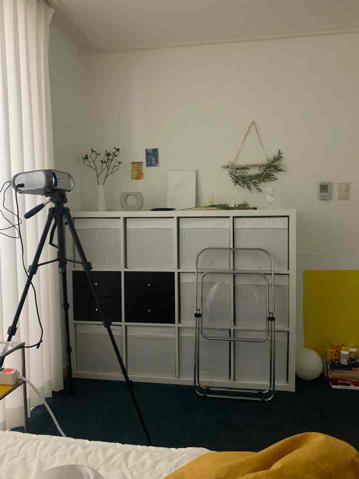 白と黒の調和がとれたワンルーム、プロジェクターと透明な折りたたみ椅子が配置されたミニマルな収納アイデアの空間