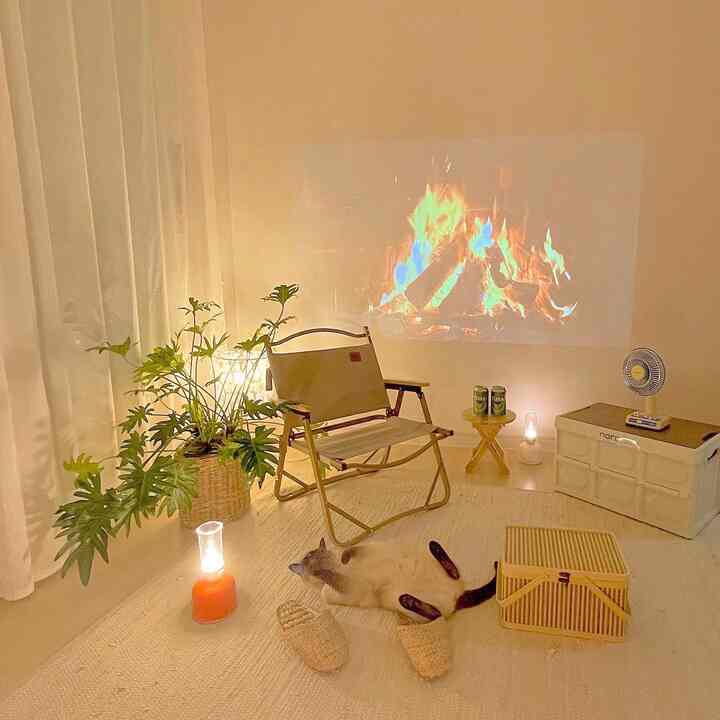 Warm beige-toned home camping space featuring a camping chair, fire video projection, cat, and plants in a cozy setting