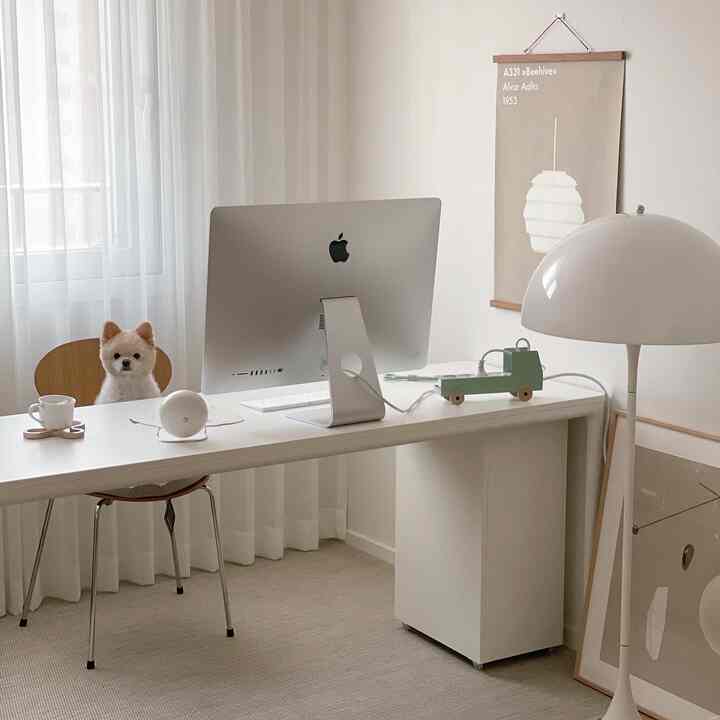 Bright white and beige toned home office study featuring an iMac on a desk and a dog sitting on a chair, creating a tidy atmosphere