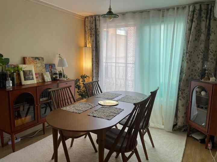 Warm wood-tone retro dining room featuring a wooden table and chairs, floral blackout curtains, and natural lighting creating a cozy atmosphere