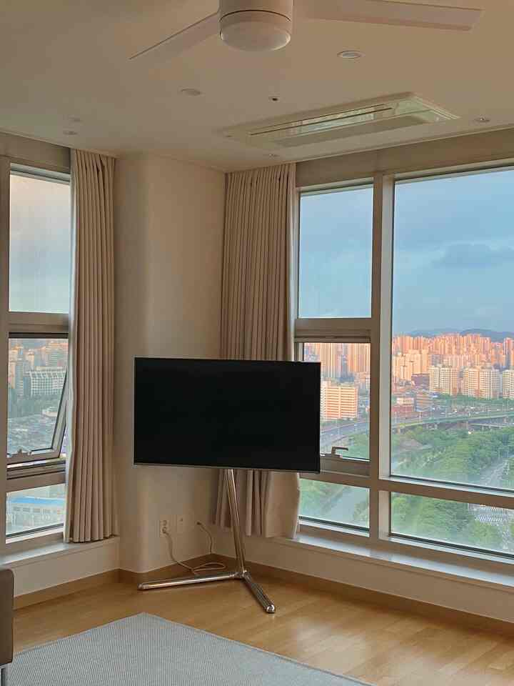 A bright and clean living room with white and wood tones, featuring thick blackout curtains and a modern TV stand