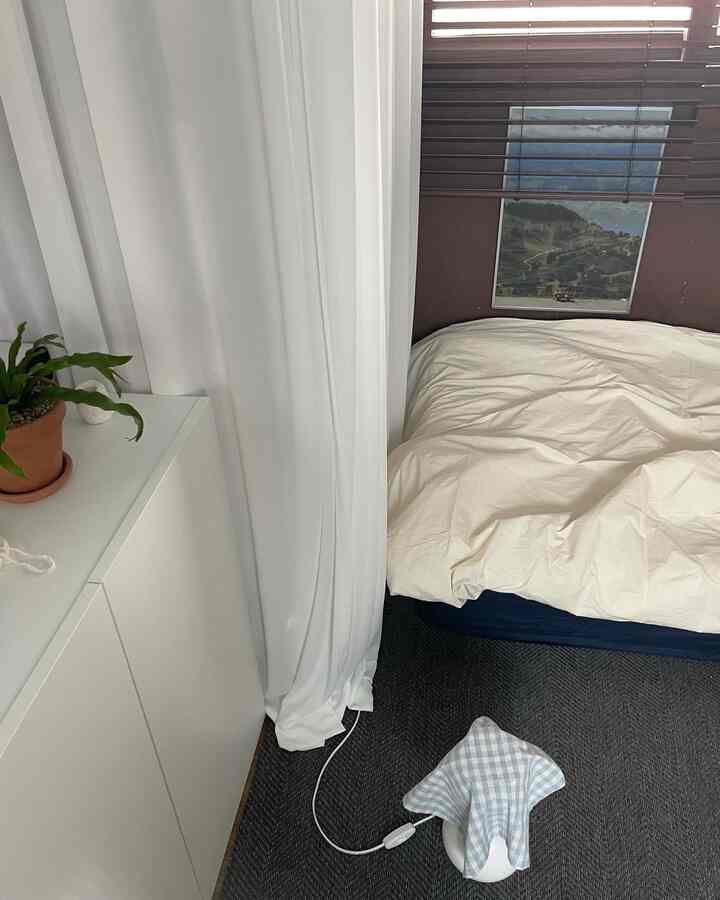 White-toned bedroom featuring neat bedding, curtains, and a plant by the window creating a cozy atmosphere