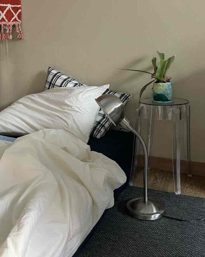 Natural beige-toned bedroom with wooden floor featuring navy bedding, transparent stool, and metal desk lamp creating a cozy atmosphere