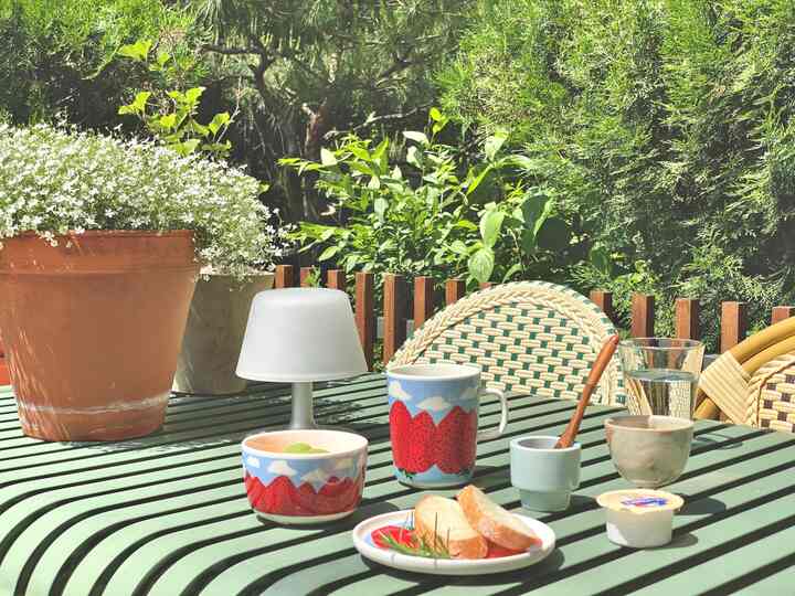 緑豊かな木々と自然素材を背景にした、緑色のテーブルと編み込みチェアが置かれた落ち着いた屋外空間