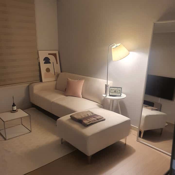 ベージュとホワイトの色調のゲストルーム、シンプルなソファとスツール、フロアランプ、全身鏡が配置された落ち着いた雰囲気のインテリア