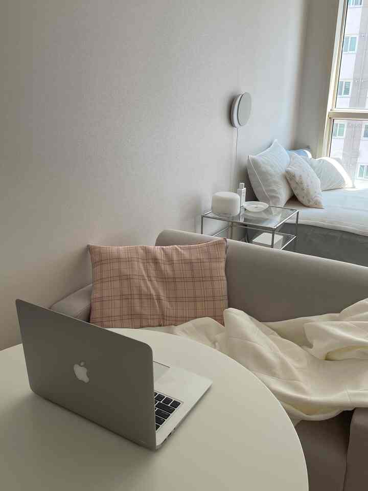 White and beige toned minimal modern living room featuring a sofa and round table with laptop, creating a cozy atmosphere