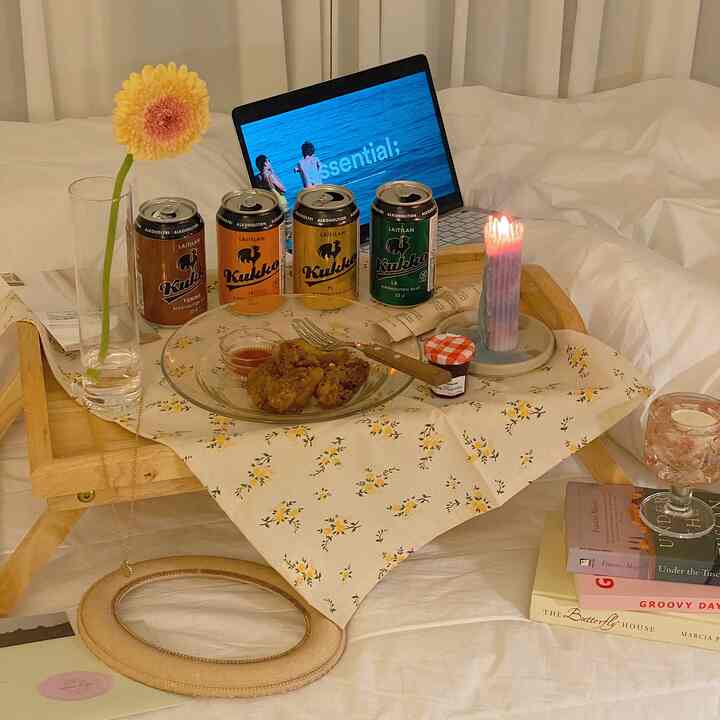 White and yellow toned bedroom featuring a wooden folding table with floral cloth, candles, food, and drinks creating a cozy atmosphere