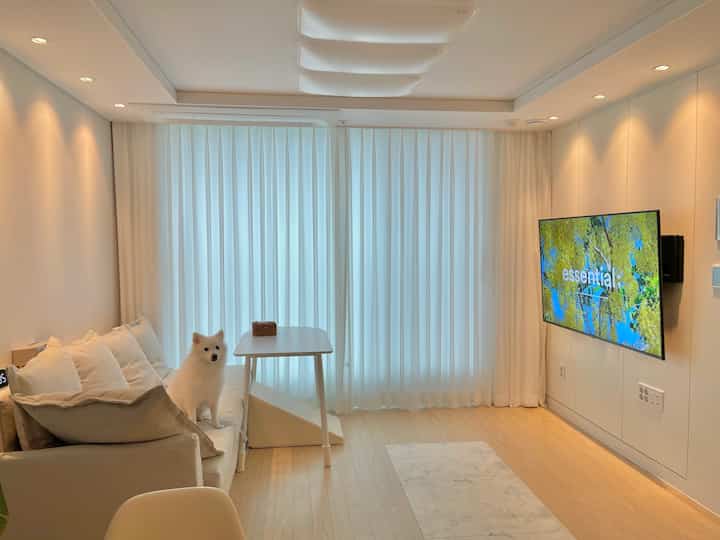 White and beige toned small living room featuring an IKEA sofa with a dog and a wall-mounted TV, clean and minimalistic