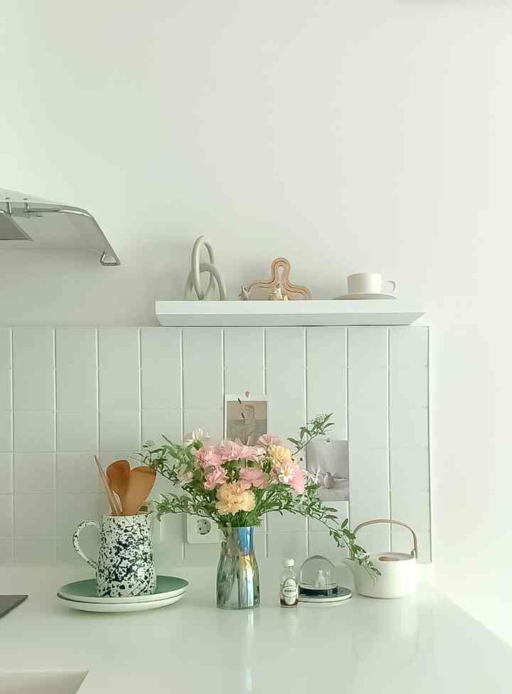 白を基調としたキッチン空間、棚上とカウンターに花や調理道具が配置された清潔で自然な雰囲気のインテリア