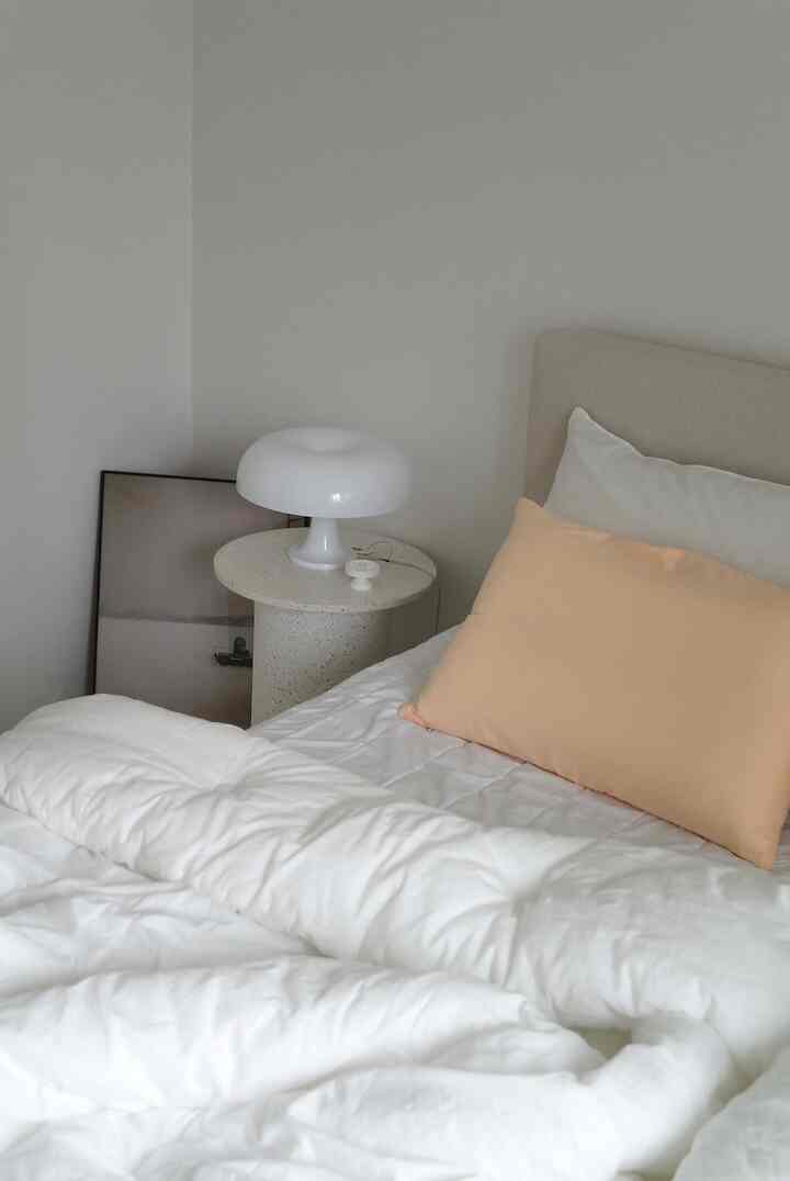 Natural beige and white toned bedroom featuring white bedding and a yellow pillow, creating a simple and cozy atmosphere