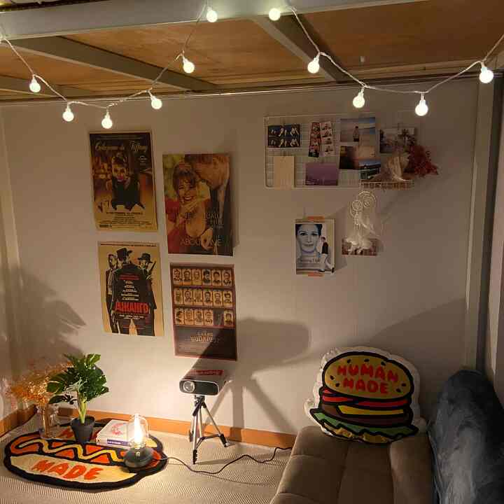 Warmly lit two-person living room featuring vintage movie posters, a projector, and string lights with a cozy cafe-style atmosphere