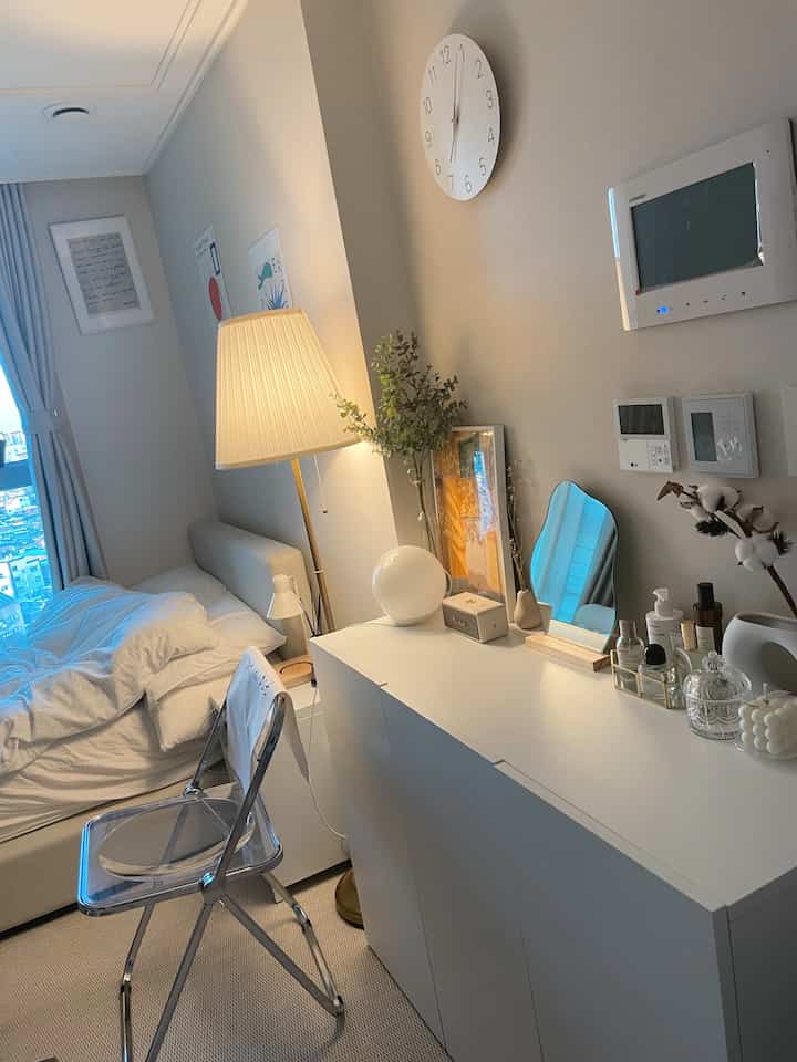 白を基調としたワンルームの寝室、ミニマルな家具とフロアランプが配置されたシンプルな雰囲気のインテリア