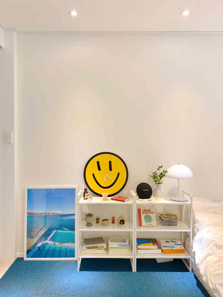 Navy and blue toned bedroom featuring a navy rug, ocean pool poster, vase with greenery, and a bright lamp creating a fresh vibe