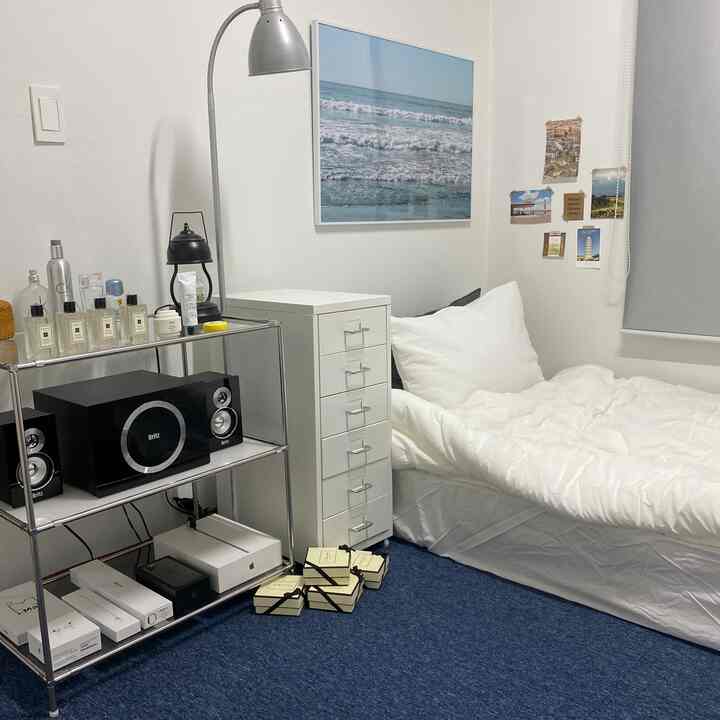 白と青のトーンのコンパクトで居心地の良い寝室、ベッドと移動式チェスト、メタルシェルフが効率的に配置されたインテリア