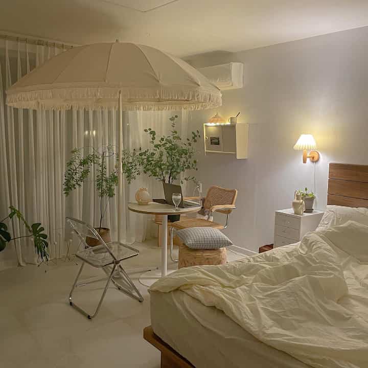 アイボリーとナチュラルな色調の寝室、中央にパラソルとラタンのアームチェア、テーブルが配置された雰囲気のある空間