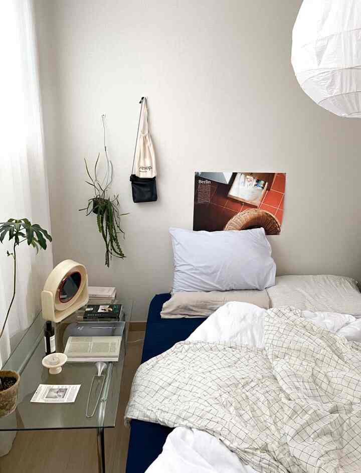 Natural-tone bedroom featuring a navy bed, white walls, glass side table, and plants by the window
