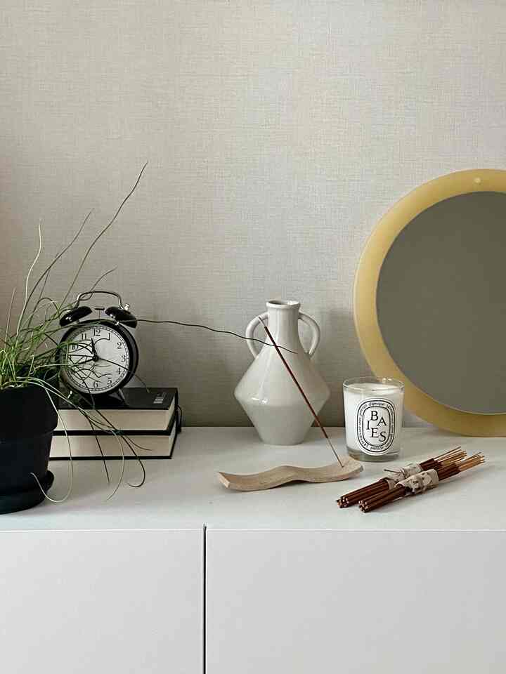 White and beige toned simple space featuring an incense holder, vase, and candle on modern interior setup