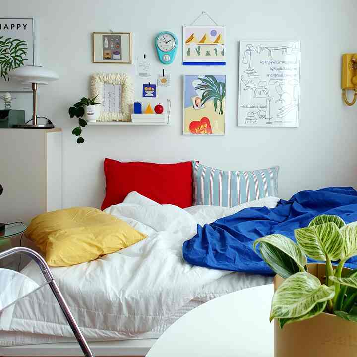 A bedroom in primary colors featuring a bed with red and yellow pillows, blue bedding, and various wall decorations creating a cozy atmosphere