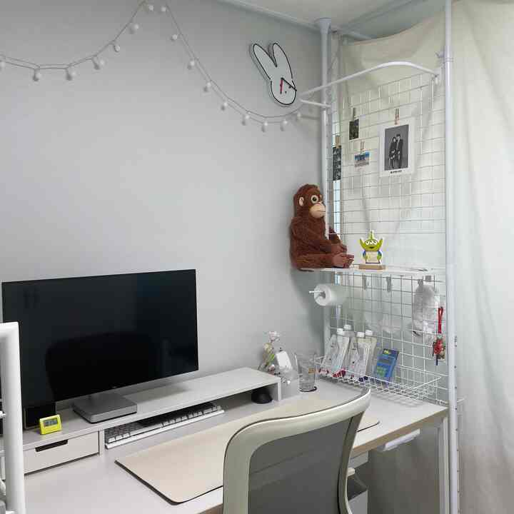 ホワイトトーンのホームオフィス、清潔感のあるデスクとモニタースタンド、整頓された収納スペースが配置された実用的な作業空間