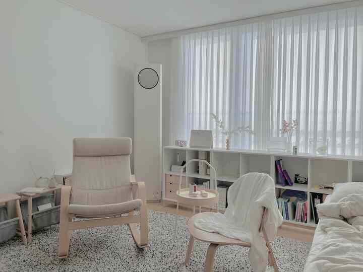 Minimal studio living room in white and wood tones featuring armchair, stool, and air conditioner