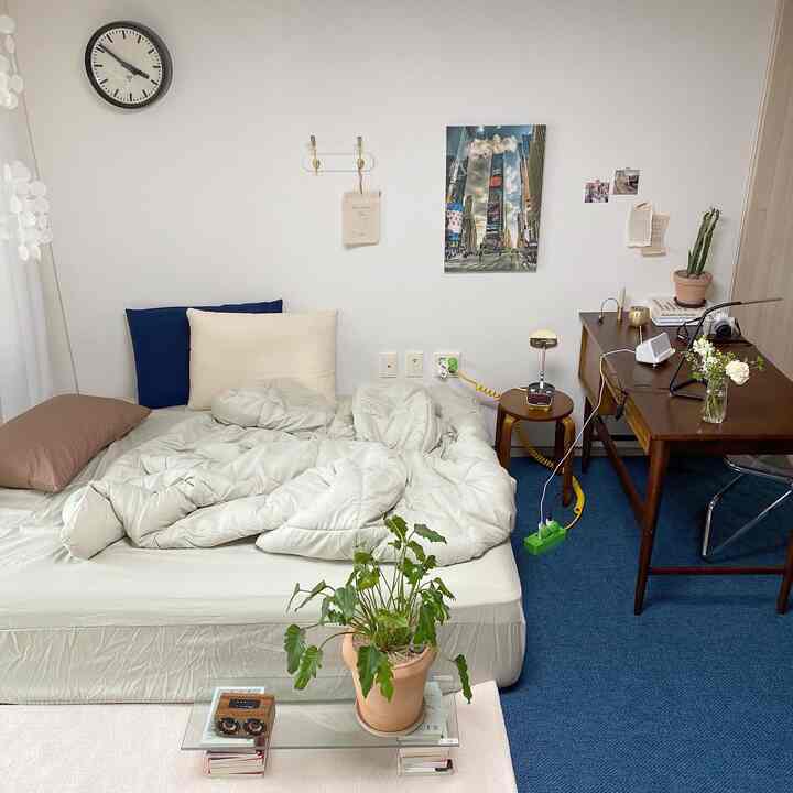 白い壁と青いラグの寝室、低床ベッドと木製デスクが配置された雰囲気のあるインテリア