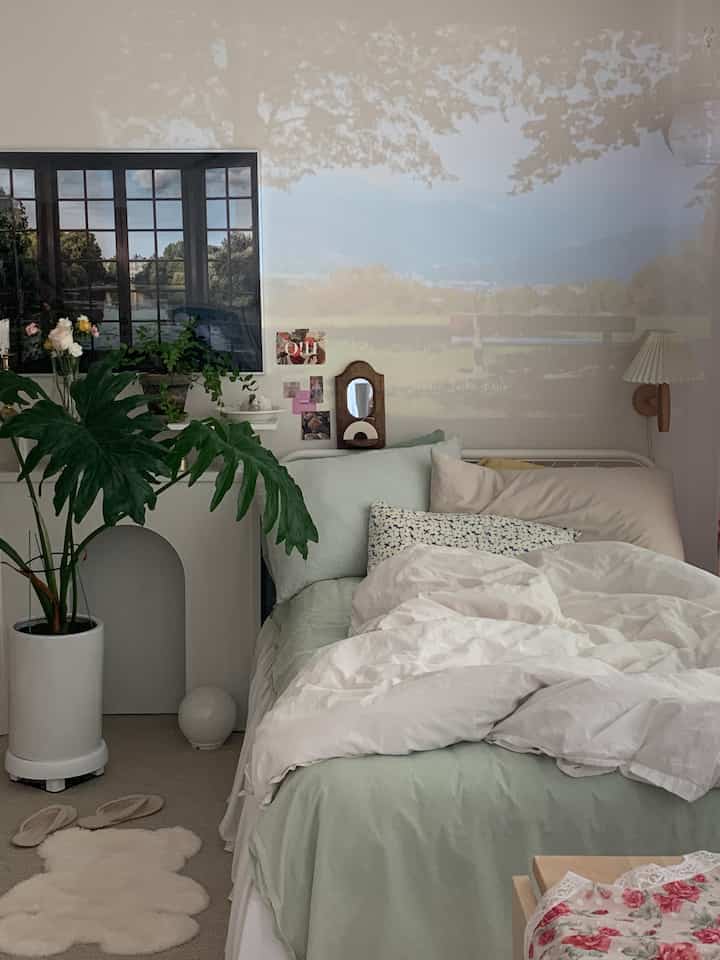Modern bedroom in white and natural tones featuring a bed, plants, and picture frames in a cozy setting