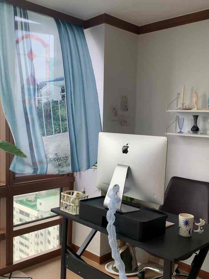 White and dark brown tone home office space featuring black desk, office chair, and blue curtains over window creating cozy atmosphere