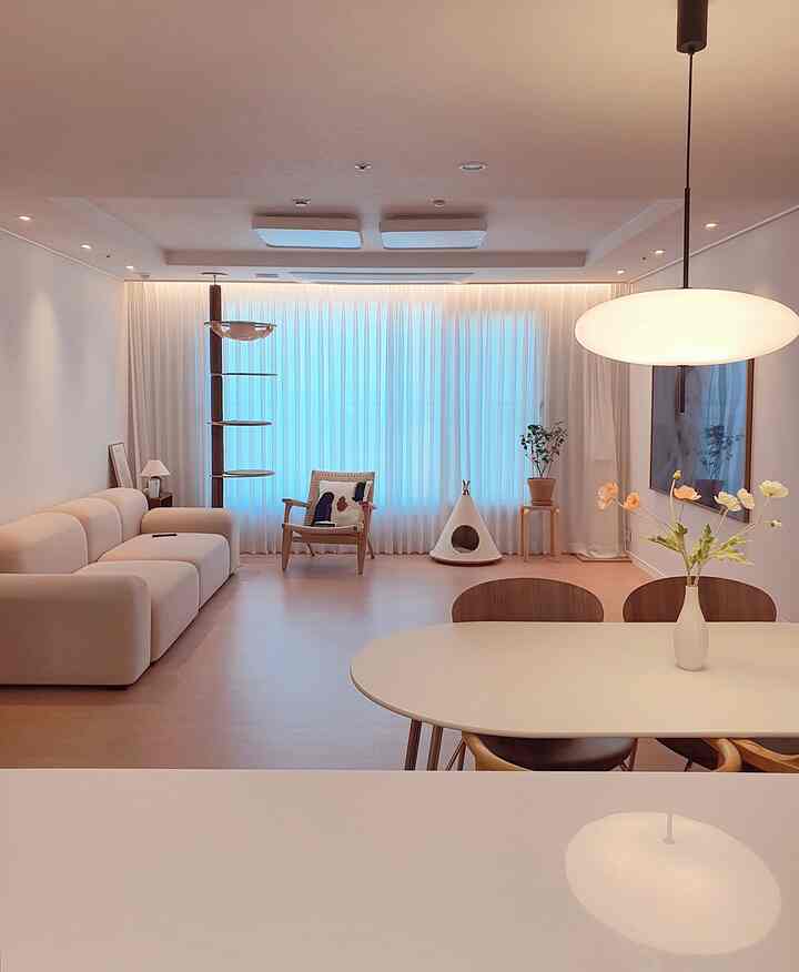 White and wood-tone living room and kitchen space featuring a cat tower and pet house with a warm, cozy atmosphere