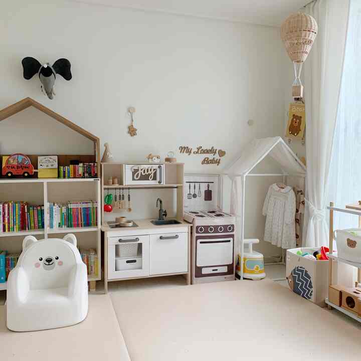 ホワイトと木目調でまとめられた子供部屋、遊び用キッチンセットとかわいいベビーチェア、本棚が配置された雰囲気のあるインテリア
