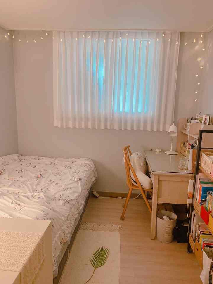 白とベージュのトーンのコンパクトな寝室、ナチュラルな木製机と椅子が配置された落ち着いた雰囲気のインテリア