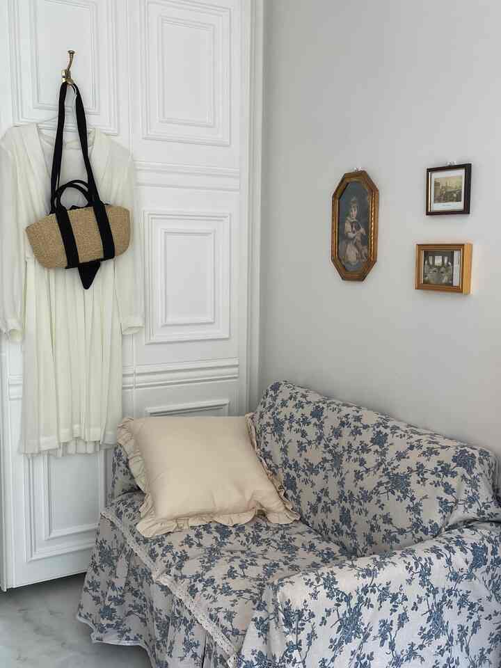 White and blue floral sofa cover in a two-person living room space, accented with vintage picture frames and beige cushion for cozy atmosphere