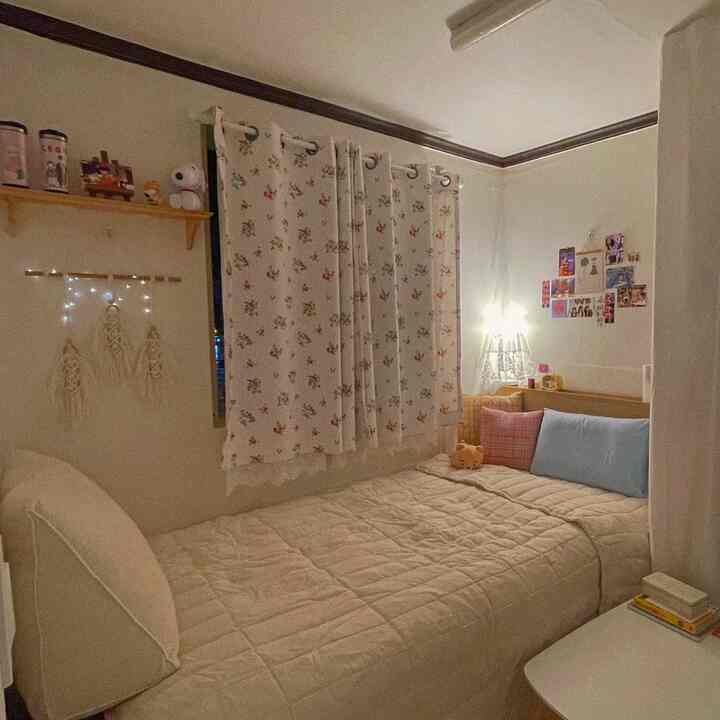 Cozy small bedroom in white and beige tones featuring floral curtains and cushions on bedding