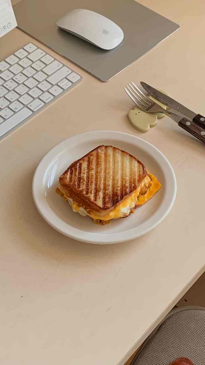 ベージュ色のデスクに白い丸皿とトーストしたチーズサンドイッチが置かれたホームオフィスの雰囲気あるインテリア。