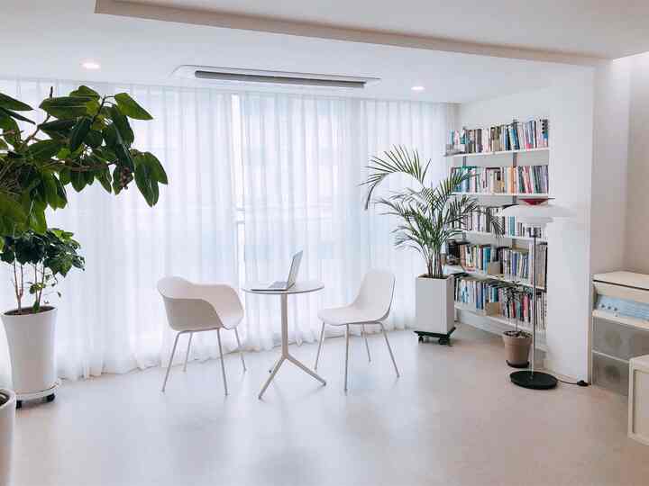 明るいホワイトトーンのダイニングルーム、小さな丸テーブルと2つの椅子、本棚が配置されたミニマルでモダンな雰囲気のインテリア