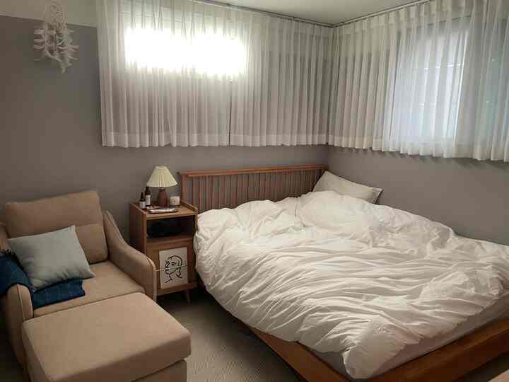 A small single bedroom in beige and white tones featuring a wooden bed and armchair creating a cozy atmosphere