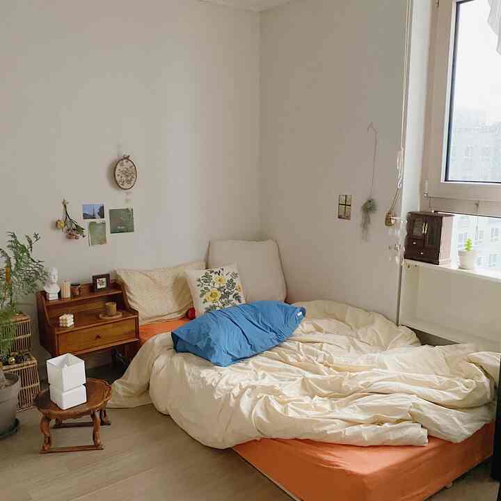 Natural tones with orange and blue accents in a studio bedroom, featuring a cozy bed and wooden nightstand in a warm atmosphere