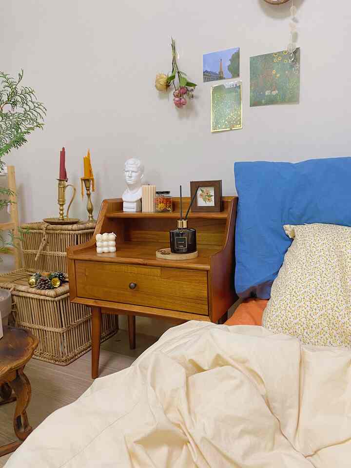 Beige bedding and blue pillow in a bedroom featuring wooden nightstand, rattan baskets, candles, and diffuser for a cozy atmosphere
