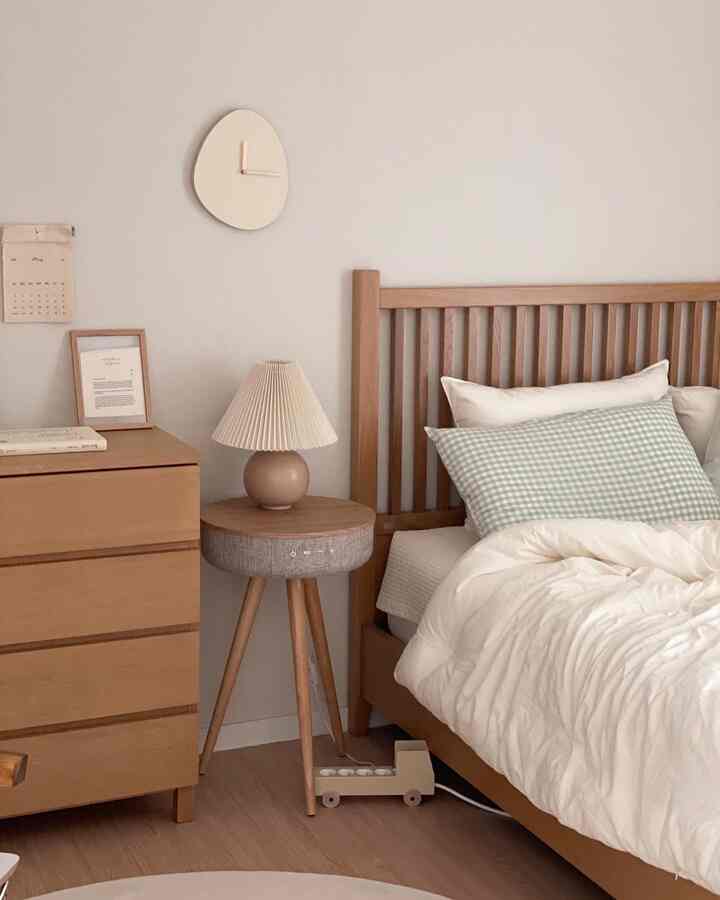 Beige and wood-toned bedroom featuring wooden bed, dresser, white bedding, and checked cushion creating a cozy atmosphere