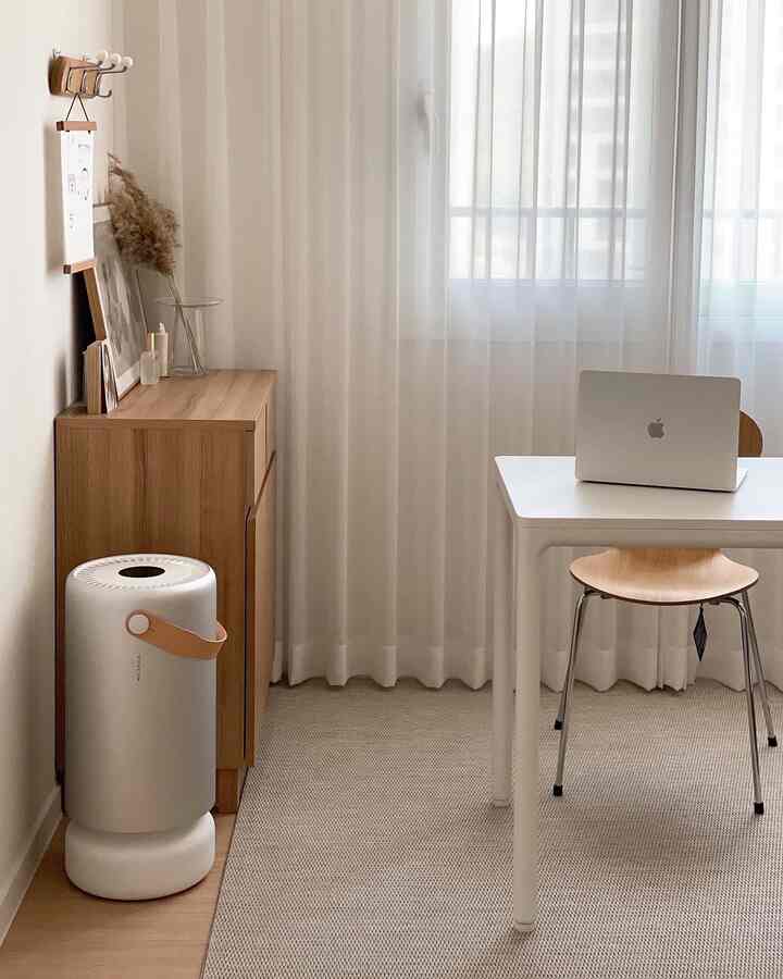 Small modern home office with white and wood tones, featuring simple furniture and sheer curtain over window
