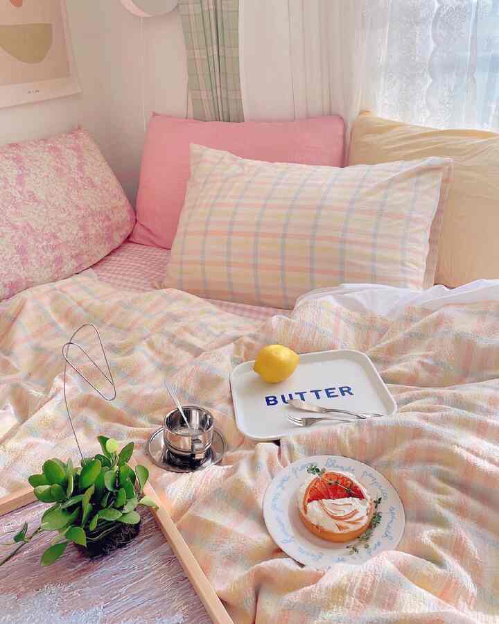 A cozy bedroom with peach and pink tones featuring soft bedding and sheer curtains, evoking a summer vibe