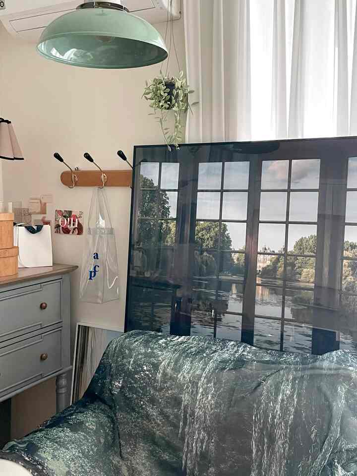 ナチュラルベージュのリビング、緑のアームチェアとヴィンテージの収納家具、白いカーテンとペンダントライトが配置された落ち着いた空間