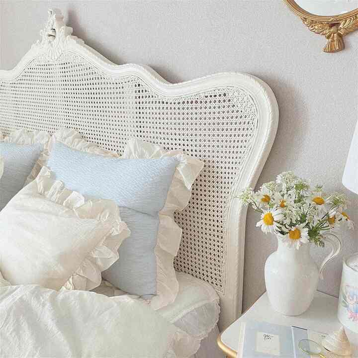 アイボリーとホワイトのトーンのフレンチカントリースタイルの寝室、レースとフリルの寝具、花瓶が配置された雰囲気のある空間