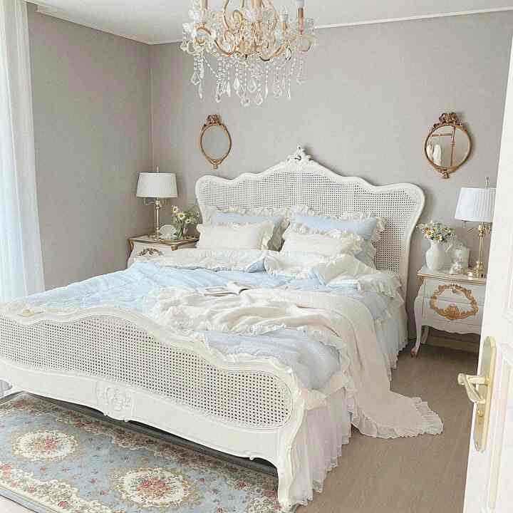 Vintage style bedroom in white and gold tones featuring an ornate bed centerpiece and table lamps on each side, creating a cozy atmosphere