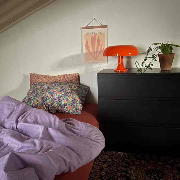 Red and purple toned loft bedroom featuring floral pillows, orange lamp, and black dresser creating cozy atmosphere
